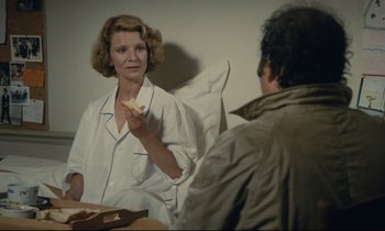Movie still from “Waiter!” (1983), directed by Claude Sautet – A woman sitting in front of a man eating a piece of food; Medium shot, Over the shoulder angle