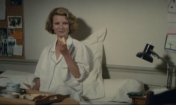 Movie still from “Waiter!” (1983), directed by Claude Sautet – A woman sitting in a chair eating a piece of bread; Medium shot, Over the shoulder angle