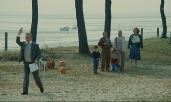Movie still from “Waiter!” (1983), directed by Claude Sautet – A group of people standing on top of a sandy beach; Extreme Wide shot, High angle