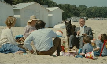 Movie still from “Waiter!” (1983), directed by Claude Sautet – A group of people sitting on the beach with a dog; Wide shot, High angle