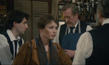 Movie still from “Waiter!” (1983), directed by Claude Sautet – A group of people standing in a room; Medium shot, Over the shoulder angle