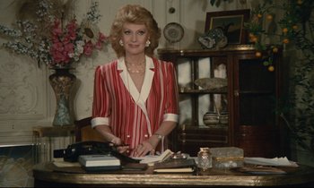 Movie still from “Waiter!” (1983), directed by Claude Sautet – An older woman standing at a desk in a room; Medium shot, Over the shoulder angle