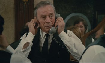 Movie still from “Waiter!” (1983), directed by Claude Sautet – An older man is holding a phone up to his ear; Close Up shot, Low angle