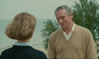 Movie still from “Waiter!” (1983), directed by Claude Sautet – A man and a woman standing next to each other on the beach; Medium shot, Over the shoulder angle