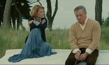 Movie still from “Waiter!” (1983), directed by Claude Sautet – A woman and a man sitting on the ground in front of a tree; Medium shot, Low angle