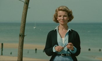 Movie still from “Waiter!” (1983), directed by Claude Sautet – A woman standing in front of the ocean holding a pair of scissors; Medium shot, Low angle