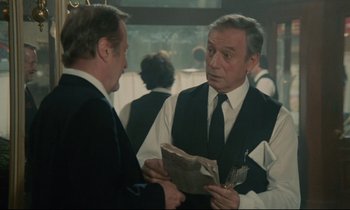 Movie still from “Waiter!” (1983), directed by Claude Sautet – Two men in suits and ties are talking to each other; Medium shot, Over the shoulder angle
