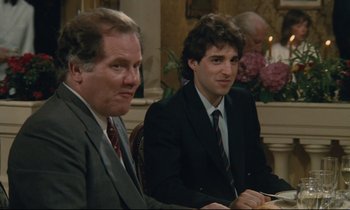 Movie still from “Waiter!” (1983), directed by Claude Sautet – Two men sitting at a table in a suit and tie; Medium shot, Over the shoulder angle