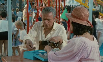Movie still from “Waiter!” (1983), directed by Claude Sautet – An older man and a young woman at an amusement park; Medium shot, Over the shoulder angle