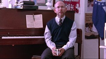 Movie still from “Waiting for Guffman” (1996), directed by Christopher Guest – A man sitting in front of a piano holding a coffee cup; Medium shot, Over the shoulder angle
