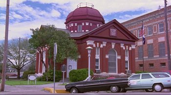 Movie still from “Waiting for Guffman” (1996), directed by Christopher Guest – A car parked in front of a red building; Extreme Wide shot, Low angle