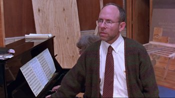 Movie still from “Waiting for Guffman” (1996), directed by Christopher Guest – A man wearing a tie and glasses sitting in front of a piano; Close Up shot, Over the shoulder angle