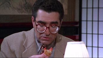 Movie still from “Waiting for Guffman” (1996), directed by Christopher Guest – A man with glasses eating a piece of food; Close Up shot, High angle