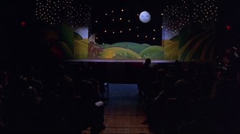 Movie still from “Waiting for Guffman” (1996), directed by Christopher Guest – People are sitting in front of a stage in a theater; Extreme Wide shot, High angle