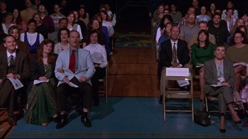 Movie still from “Waiting for Guffman” (1996), directed by Christopher Guest – A group of people sitting in chairs in front of a crowd; Wide shot, High angle