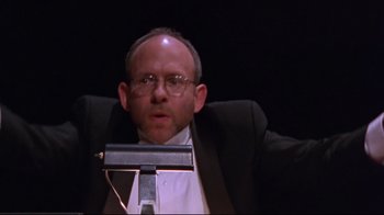 Movie still from “Waiting for Guffman” (1996), directed by Christopher Guest – A man in a suit and glasses sitting in a chair; Close Up shot, Low angle