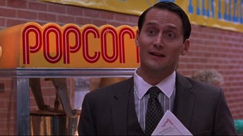 Movie still from “Waiting for Guffman” (1996), directed by Christopher Guest – A man in a suit and tie holding a popcorn machine; Close Up shot, Low angle