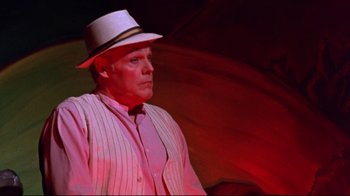 Movie still from “Waiting for Guffman” (1996), directed by Christopher Guest – A man in a hat and a striped shirt is holding an umbrella; Medium shot, Low angle