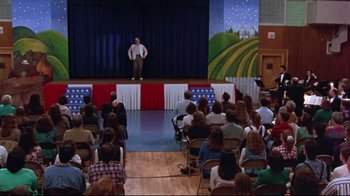 Movie still from “Waiting for Guffman” (1996), directed by Christopher Guest – A man standing on a stage in front of a group of people; Extreme Wide shot, High angle