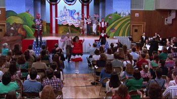 Movie still from “Waiting for Guffman” (1996), directed by Christopher Guest – A group of people sitting and standing in front of a crowd; Extreme Wide shot, High angle