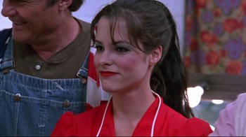 Movie still from “Waiting for Guffman” (1996), directed by Christopher Guest – A woman in a red dress with red lipstick and a ponytail; Close Up shot, Over the shoulder angle
