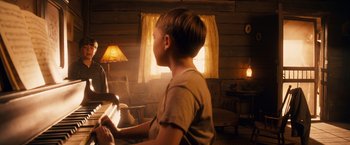 Movie still from “Walk Hard: The Dewey Cox Story” (2007), directed by Jake Kasdan – A young boy is playing the piano in a cabin; Medium shot, Over the shoulder angle