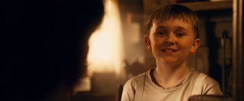 Movie still from “Walk Hard: The Dewey Cox Story” (2007), directed by Jake Kasdan – A young boy is smiling for the camera in front of a fireplace; Close Up shot, Over the shoulder angle