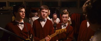 Movie still from “Walk Hard: The Dewey Cox Story” (2007), directed by Jake Kasdan – Two young men are standing in front of a group of young people; Medium shot, Over the shoulder angle