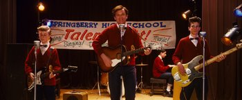 Movie still from “Walk Hard: The Dewey Cox Story” (2007), directed by Jake Kasdan – A man holding a guitar on stage in front of an audience; Medium shot, High angle