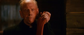Movie still from “Walk Hard: The Dewey Cox Story” (2007), directed by Jake Kasdan – An older man wearing a priest's outfit holding a red ribbon; Close Up shot, Low angle