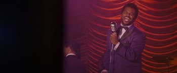 Movie still from “Walk Hard: The Dewey Cox Story” (2007), directed by Jake Kasdan – A man in a purple suit holding a microphone; Close Up shot, Over the shoulder angle