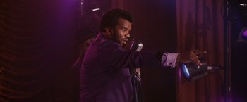 Movie still from “Walk Hard: The Dewey Cox Story” (2007), directed by Jake Kasdan – A man holding a microphone in front of a crowd; Medium shot, Over the shoulder angle