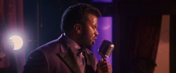Movie still from “Walk Hard: The Dewey Cox Story” (2007), directed by Jake Kasdan – A man in a purple jacket is singing into a microphone; Close Up shot, Over the shoulder angle