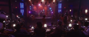 Movie still from “Walk Hard: The Dewey Cox Story” (2007), directed by Jake Kasdan – A group of people sitting at tables in front of a stage; Extreme Wide shot, High angle