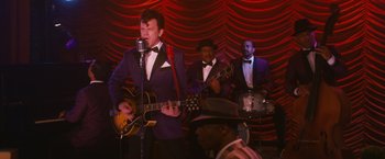 Movie still from “Walk Hard: The Dewey Cox Story” (2007), directed by Jake Kasdan – A group of men in tuxedos and hats playing musical instruments; Medium shot, Over the shoulder angle