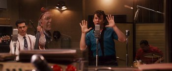 Movie still from “Walk Hard: The Dewey Cox Story” (2007), directed by Jake Kasdan – A man in a recording studio with his hands up; Medium shot, Over the shoulder angle