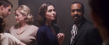 Movie still from “Walk Hard: The Dewey Cox Story” (2007), directed by Jake Kasdan – A woman standing next to a man holding a cigarette in her mouth; Medium shot, Low angle