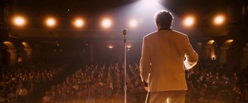 Movie still from “Walk Hard: The Dewey Cox Story” (2007), directed by Jake Kasdan – A man standing on a microphone in front of an audience; Wide shot, Low angle