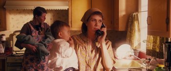 Movie still from “Walk Hard: The Dewey Cox Story” (2007), directed by Jake Kasdan – A woman holding a baby while on the phone; Medium shot, High angle