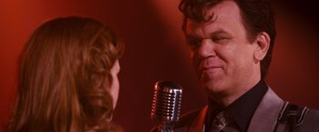 Movie still from “Walk Hard: The Dewey Cox Story” (2007), directed by Jake Kasdan – A man and a woman talking to each other in front of a microphone; Close Up shot, Over the shoulder angle