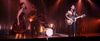 Movie still from “Walk Hard: The Dewey Cox Story” (2007), directed by Jake Kasdan – A group of people playing instruments on a stage; Medium shot, Over the shoulder angle