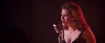 Movie still from “Walk Hard: The Dewey Cox Story” (2007), directed by Jake Kasdan – A woman is singing into an old fashioned microphone; Close Up shot, Over the shoulder angle