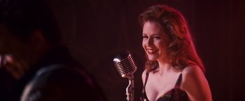 A beautiful woman standing next to an old fashioned microphone