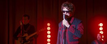 Movie still from “Walk Hard: The Dewey Cox Story” (2007), directed by Jake Kasdan – A man in a red jacket is holding a microphone; Medium shot, Low angle