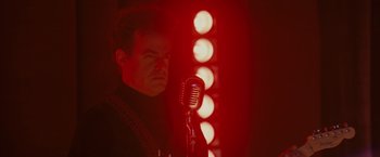 Movie still from “Walk Hard: The Dewey Cox Story” (2007), directed by Jake Kasdan – A man standing in front of a microphone in front of lights; Medium shot, Low angle