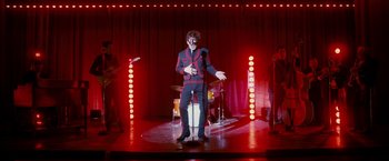 Movie still from “Walk Hard: The Dewey Cox Story” (2007), directed by Jake Kasdan – A man standing on a stage in front of a microphone; Wide shot, Low angle