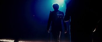 Movie still from “Walk Hard: The Dewey Cox Story” (2007), directed by Jake Kasdan – A man in a suit walking in a dark room; Wide shot, Low angle