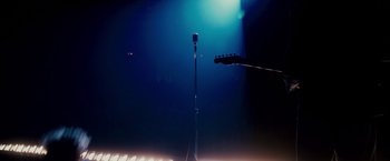 Movie still from “Walk Hard: The Dewey Cox Story” (2007), directed by Jake Kasdan – A microphone and a guitar on a stage lit by a blue light; Medium shot, Low angle