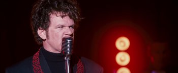 Movie still from “Walk Hard: The Dewey Cox Story” (2007), directed by Jake Kasdan – A man with curly hair is singing into a microphone; Close Up shot, Low angle
