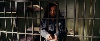 Movie still from “Walk Hard: The Dewey Cox Story” (2007), directed by Jake Kasdan – A man standing behind bars in a jail cell; Medium shot, High angle